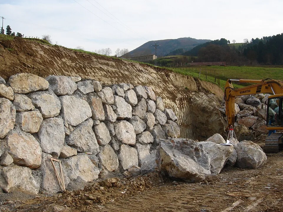 Large stone blocks stacked as a retaining wall, with an excavator beside the wall